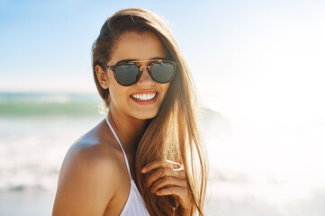 Woman, portrait and sunglasses by ocean for holiday, vacation and summer adventure on beach outdoor. Tourist, nature and Miami for smile, confidence and weekend travel with swimsuit for happiness