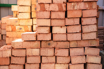 Fototapeta premium Stack of red bricks on concrete foundation, process of house building. Concrete foundation with bricks for laying. Building materials at construction