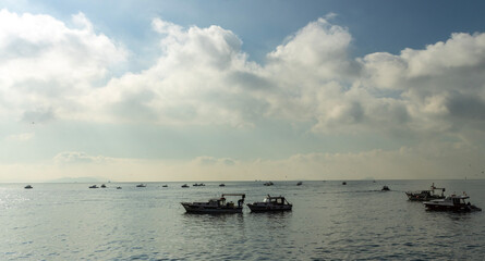 A serene moment on Istanbul's Bosphorus with a group of fishing boats anchored, silhouetted against a hazy sky. The boats, with their simple design, speak of the region's enduring fishing tradition.