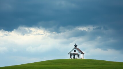 Fototapeta premium Small white church is on a hilltop in a field. The sky is cloudy and the weather is overcast