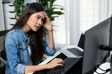 Young Asian IT developer analyzing online software development information on pc screens and laptop, creating program coding for latest version application on website with firmware updated. Stratagem.