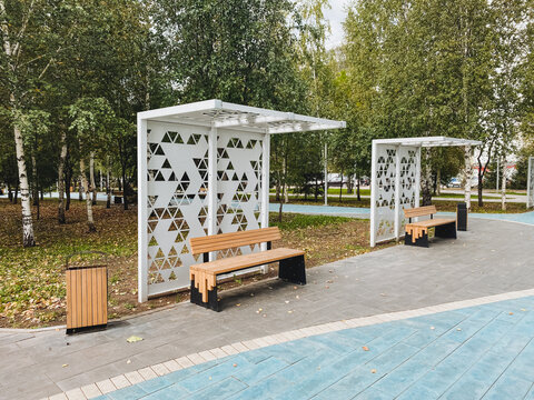 There is a beautiful park featuring a long row of benches where visitors can sit and relax, along with a conveniently placed trash can for maintaining cleanliness in the area