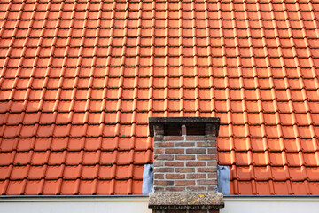 Part of a Dutch roof with red roof tiles and a brick chimney.