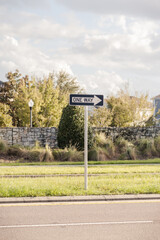 ONE WAY sign in the middle of the road with trees and brick wall in the background on a sunny day in the USA