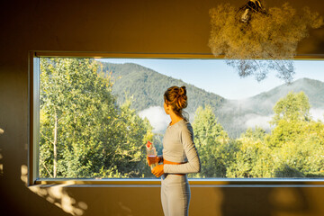 A woman in light activewear takes a refreshing sip of water after her morning yoga session. The...