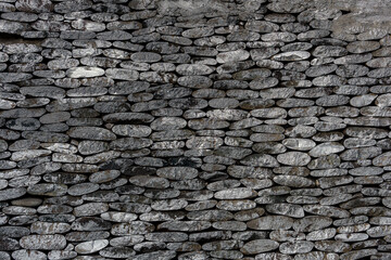 Stone wall made of stacked flat stones arranged horizontally. The stones fit snugly against each other, creating a tightly packed and uniform appearance.