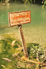 A rusty sign saying "Do not swim in this area" at the pools of the Kuang Si Falls, Waterfalls, close to Luang Prabang, Laos