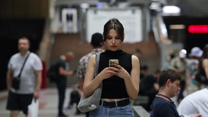 Stylish young woman reading a text message on her mobile phone while waiting for a subway train