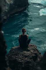 Fototapeta premium A woman sits cross-legged meditating on a cliff, overlooking the vast ocean, symbolizing peace and introspection.