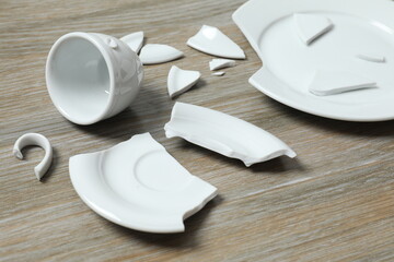 White cup and plate broken on wooden background