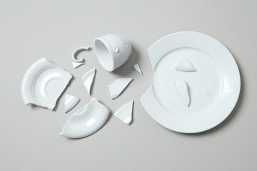 White cup and plate broken on gray background