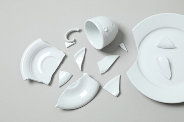 White cup and plate broken on gray background