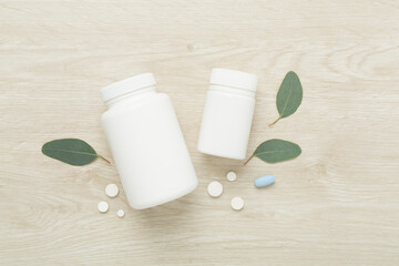 Bottles with pills and green leaves on wooden background, top view