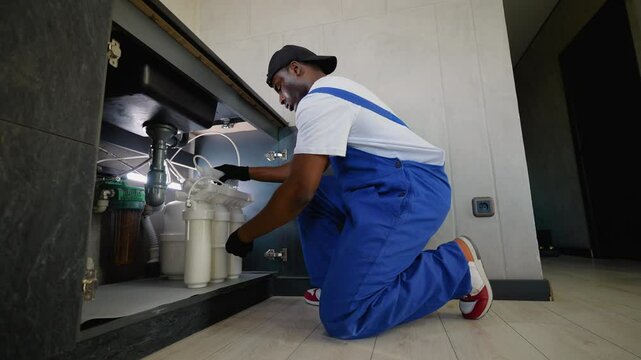 African American plumber setting up a reverse osmosis water filtration system under a kitchen sink
