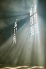 Vertical low angle shot of sun rays through huge vertical church windows cutting strong fog