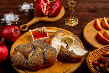 Challah, honey, apple and pomegranate and burning candles on the table with the menorah Rosh Hashanah