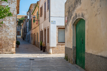 Obraz premium Narrow alley in Alcudia, Mallorca with potted plants in front of the homes during great weather, majorca spain