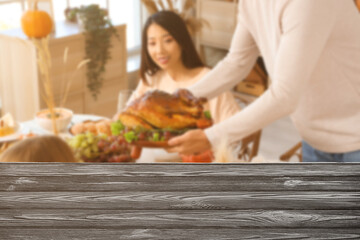 Young man bringing tasty turkey to dining table with his friends at home on Thanksgiving Day