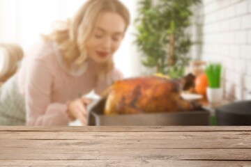 Empty wooden table and young housewife cooking tasty turkey in kitchen