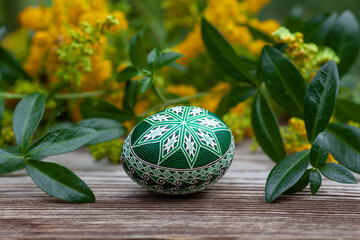 Green easter egg on a wooden surface on a background of yellow flowers