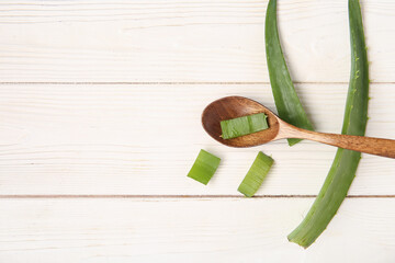 Aloe vera leaves and spoon on white wooden background