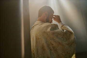 Back view of Caucasian priest in golden white robe adjusting his round glasses before church service