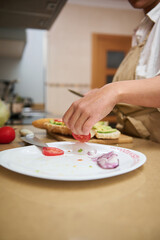 A person in a cozy kitchen prepares a healthy meal with fresh vegetables, slicing tomatoes and onions for a delicious sandwich. The scene captures the joy of cooking with natural ingredients at home.
