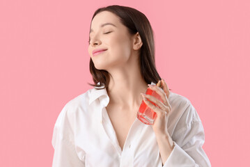 Beautiful young woman applying perfume on pink background, closeup