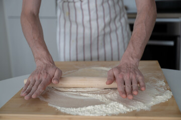 man using rolling pin for yeast dough in the domestic kitchen