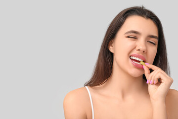 Woman with beautiful lips eating tasty candy on grey background