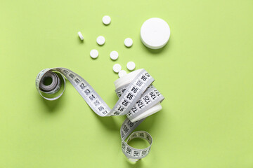 Bottle with weight loss pills and measuring tape on green background