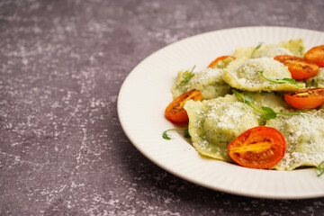 Plate of tasty ravioli with tomatoes and cheese on grey background