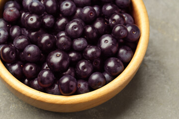 Ripe acai berries in bowl on grey textured table, above view