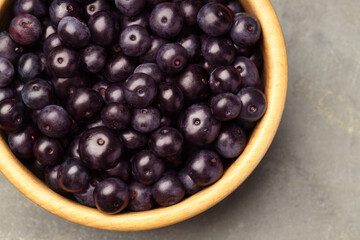 Ripe acai berries in bowl on grey textured table, top view. Space for text