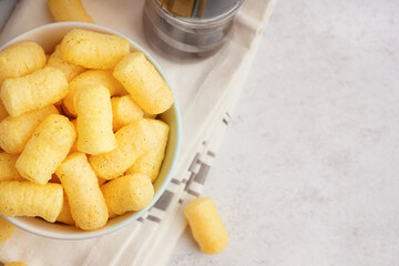Bowl with tasty salty corn sticks on light background, closeup
