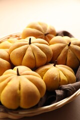 Wicker basket with tasty pumpkin shaped buns on beige background, closeup
