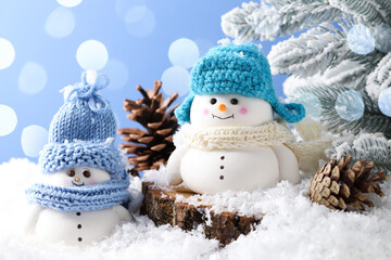 Cute decorative snowmen, fir tree branches and cones on artificial snow against light blue background, closeup
