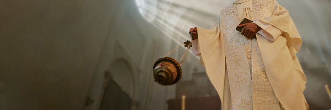 Website banner with unrecognizable priest holding Bible and majestic golden censer while besmoking nave