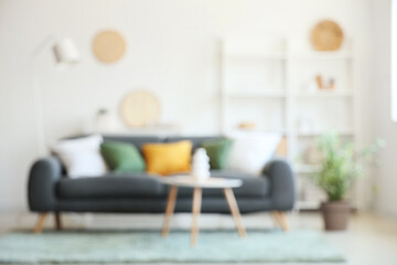 Comfortable sofa with cushions and coffee table with vase in interior of living room. Blurred view