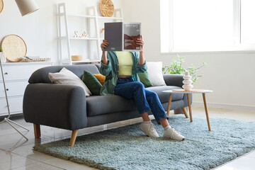 Young woman with magazine sitting on sofa in interior of living room