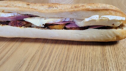 Sandwich de pain montagnard,  fromage, pommes de terre, bœuf, posé sur table en bois