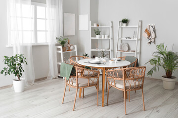 Served dining table with wicker chairs and shelving units in interior of stylish kitchen