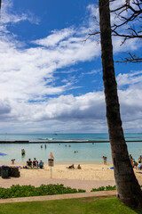 people playing in the ocean water and relaxing in the sand at Waikiki Beach with lush green palm trees and clouds in Honolulu Hawaii USA