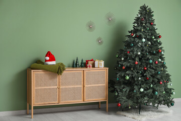 Decorated Christmas tree, chest of drawers with decor, gifts, plaid and Santa hat in interior of living room