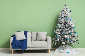 Cozy sofa with plaid and decorated Christmas tree near green wall in room