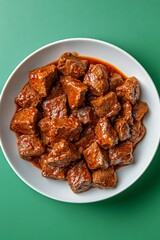 Tender beef chunks in rich sauce served on a white plate against a vibrant green background
