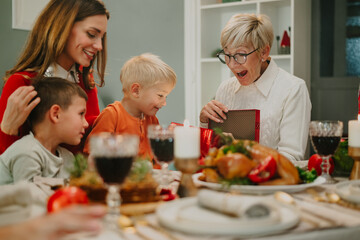 Family having christmas dinner together while grandmother opening gifts
