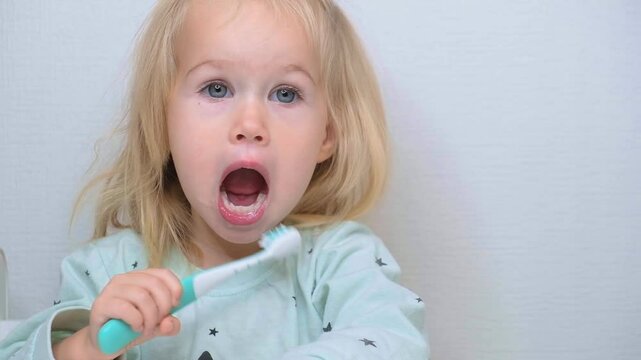 Little child toddler girl two-year-old brushing her teeth with an electric toothbrush.