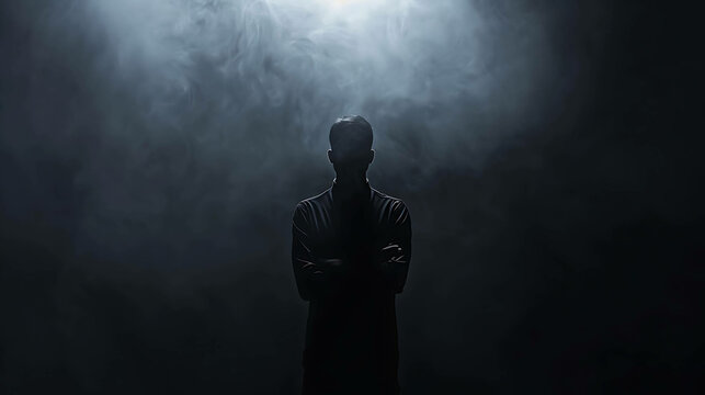 A mysterious man stands in the darkness, his face obscured by shadows. He is wearing a dark suit and has his arms crossed.