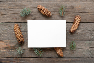 Christmas composition with fir tree branches, cones and blank card on wooden background. Top view